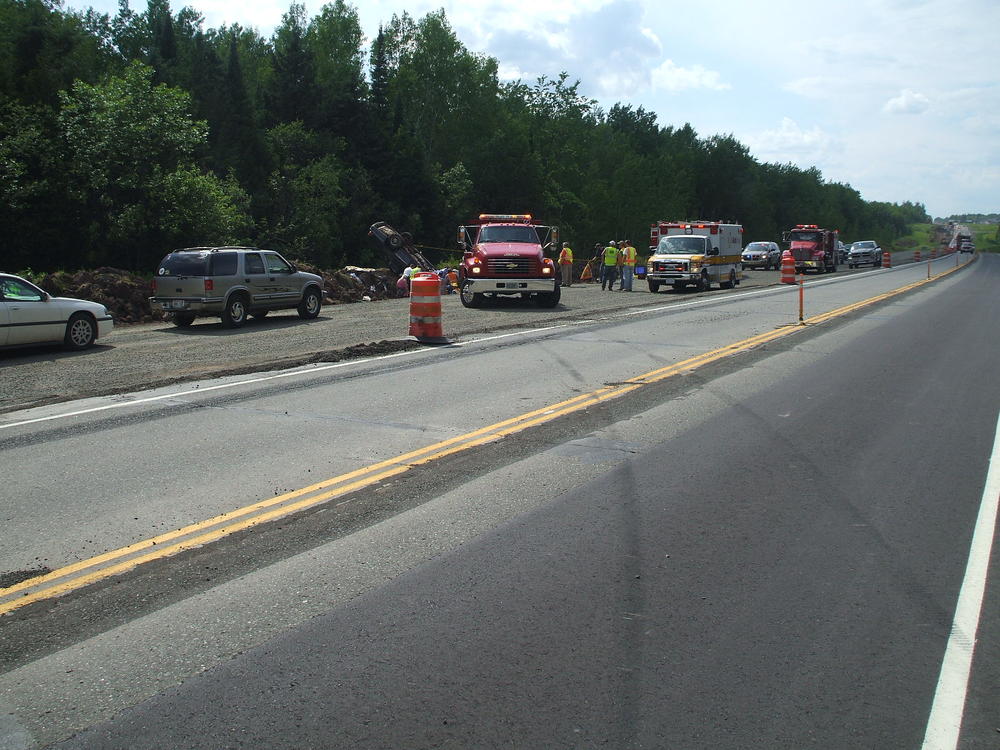 tire marks on the road, emergency vehicles alongside the road while trying to flip a car back over